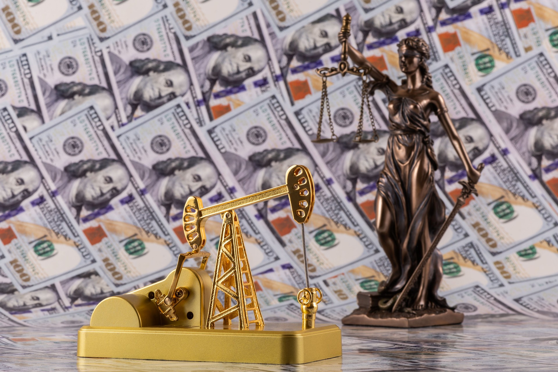 Themis figure and a miniature oil pump against the background of 100 US dollar bills