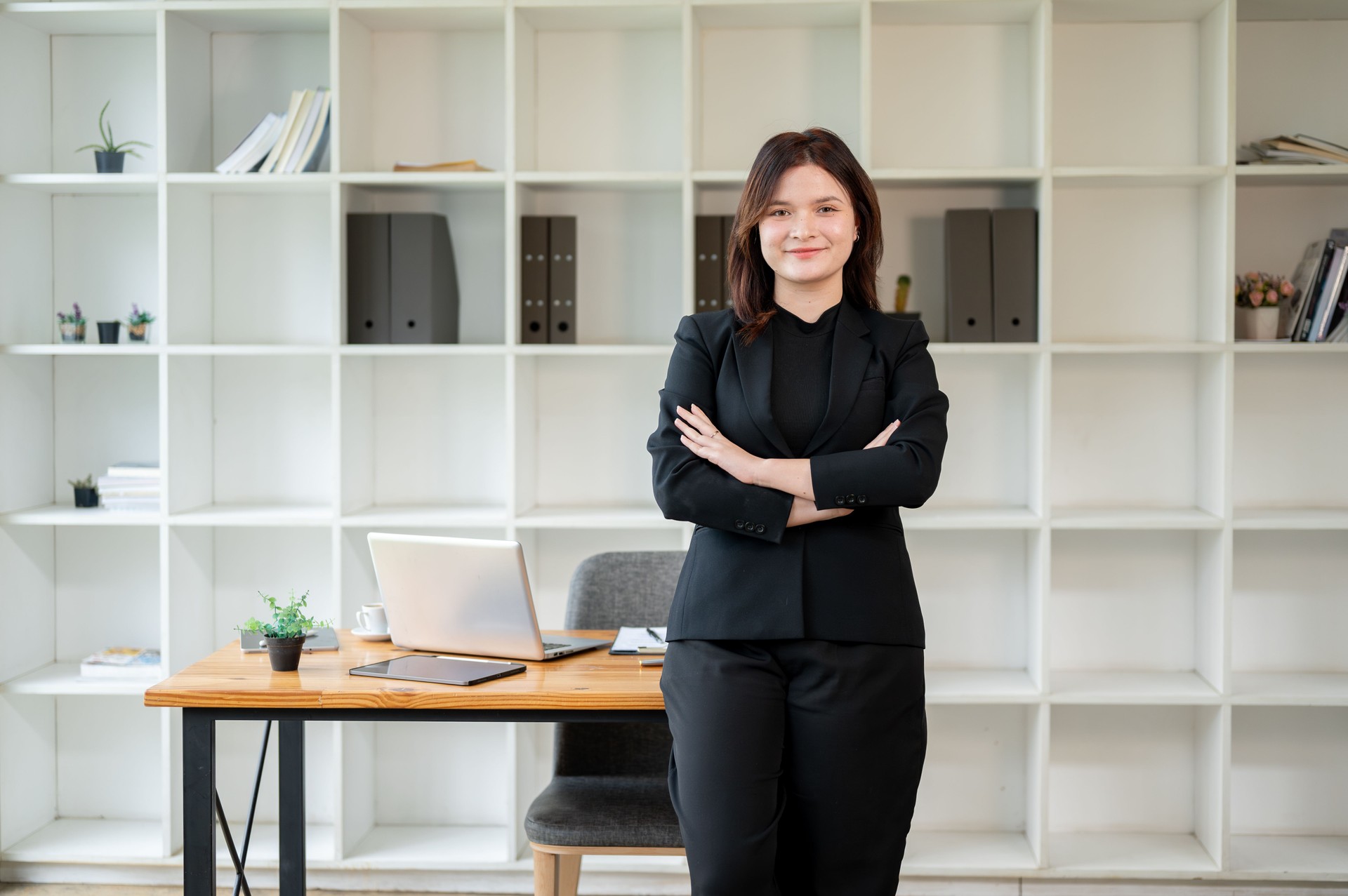 A confident businesswoman standing in her office with her arms crossed, looking at the camera.
